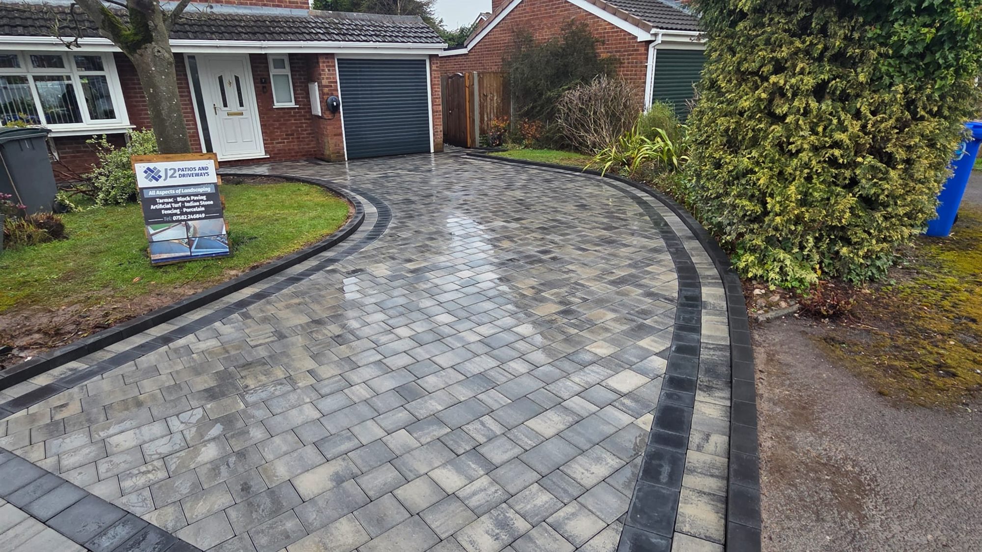 A curved block paved driveway with a charcoal border, sweeping up to a detached house