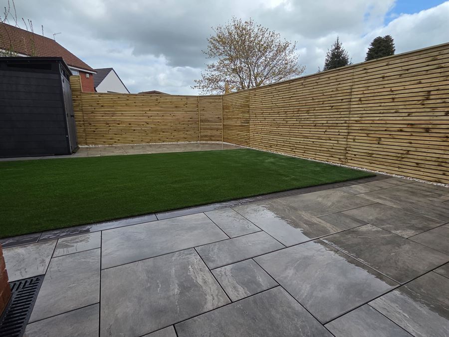 A garden boundary in new horizontal slatted timber fencing, beside an artificial lawn and porcelain patio