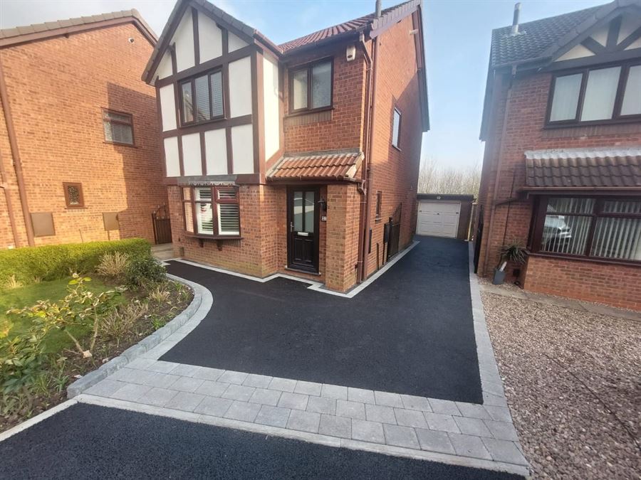 A freshly laid tarmac driveway with a block paved edge outside a detached house
